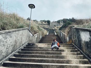 Low angle view of boy sitting on steps against sky