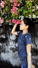 Teenage girl touching flowers while standing against retaining wall