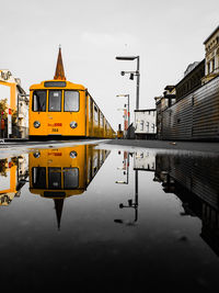 Reflection of train in puddle on street against sky