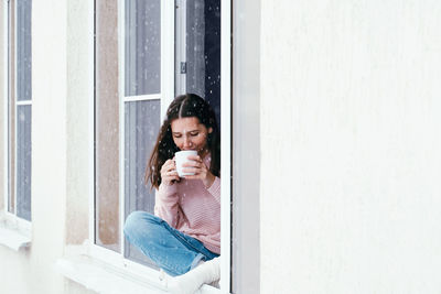 Young woman holding camera on window