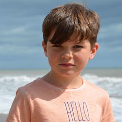 Close-up portrait of boy standing at beach against sky