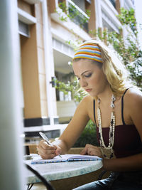 Young woman writing in diary while sitting at table