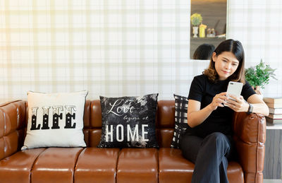 Young woman using mobile phone while sitting on sofa