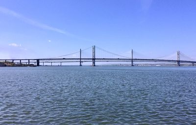 Side view of the suspension forth road bridge over sea against blue sky