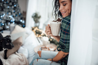 Smiling woman holding hot chocolate while sitting at home