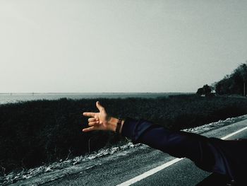 Midsection of man pointing at shore against clear sky