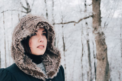 Close-up of woman wearing fur coat standing against trees during winter