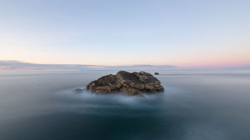 Rocks in sea against sky during sunset