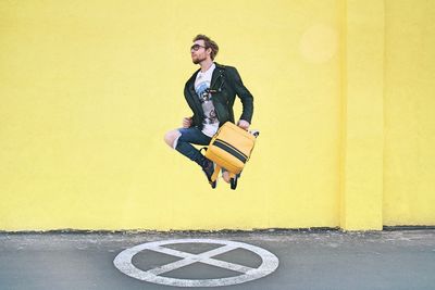 Young man with backpack jumping against wall
