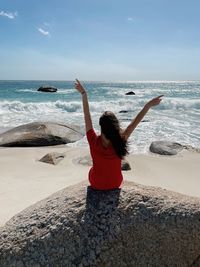 Rear view of woman standing at beach against sky