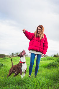 Woman with dog standing on grass field against sky