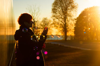 Side view of silhouette woman holding plant against sky during sunset