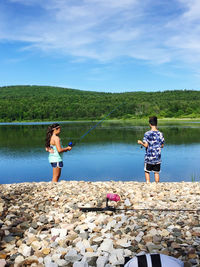Rear view of woman standing by lake against sky