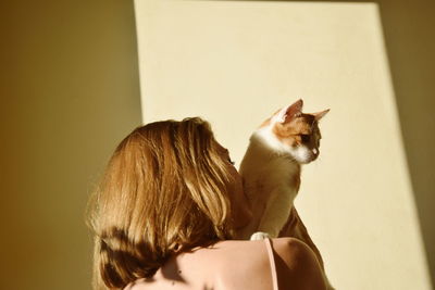 Low angle view of woman with cat against wall
