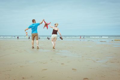 Rear view of playful parents swinging child at beach against sky