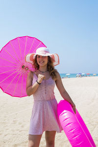 Portrait of woman holding umbrella and pool raft at beach