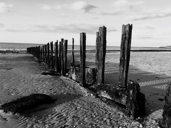 Wooden posts on beach against sky