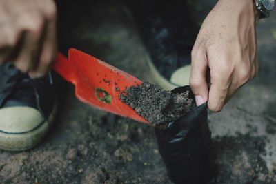 Low section of person filling plastic bag with soil on field