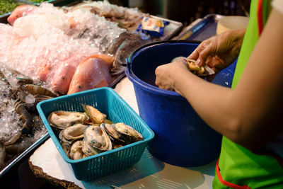 Midsection of vendor cleaning oysters at fish market