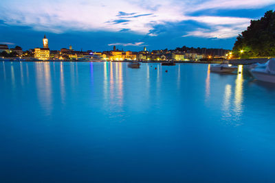 Illuminated buildings by sea against blue sky at dusk
