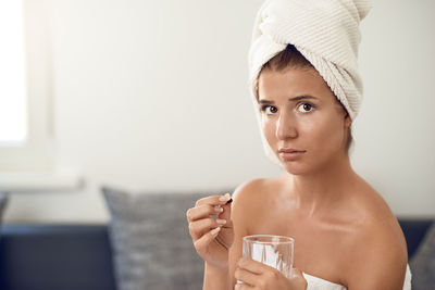 Portrait of young woman wearing bathrobe taking medicine while sitting on sofa at home