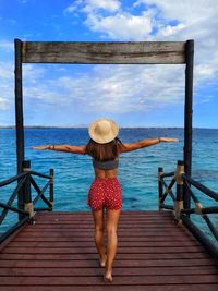 Rear view of woman walking on pier over sea against sky