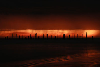 Silhouette wooden posts on sea against sky at sunset