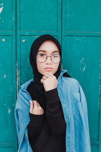 Portrait of young woman standing against blue door