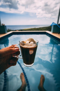 Cropped hand of woman holding drink by swimming pool