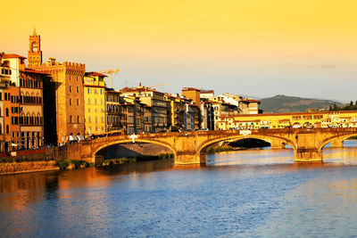 Arch bridges over arno river by buildings against sky
