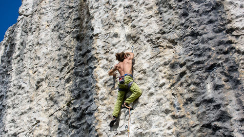 Rear view of shirtless man climbing on rock