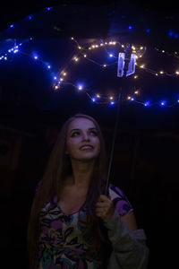Portrait of smiling woman holding illuminated light at night