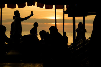 Silhouette people by sea against sky during sunset