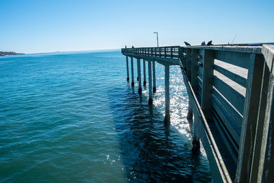 Pier over sea against clear blue sky