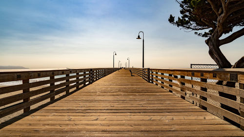Wooden footbridge over sea against sky during sunset