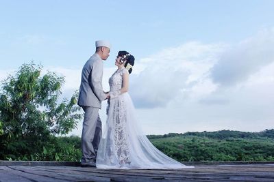 Rear view of man and woman with arms outstretched against sky