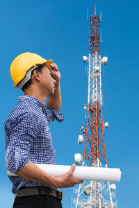 Low angle view of engineer standing against communications tower