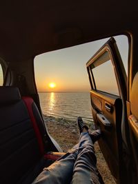 Low section of person in sea against sky during sunset