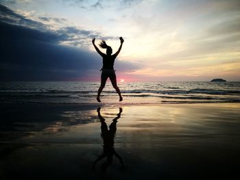 Full length of silhouette woman jumping at beach during sunset