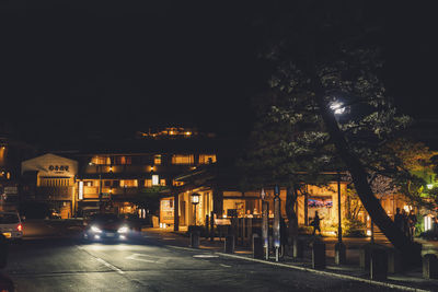 Illuminated street by buildings in city at night