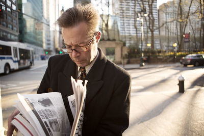 Businessman reading newspaper while standing on footpath