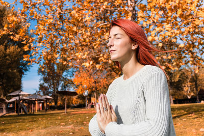 Young woman looking away while standing by tree during autumn