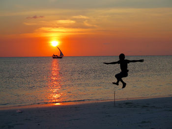 Silhouette playful boy jumping at beach against sky during sunset