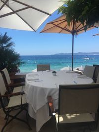 Empty chairs and tables by swimming pool against sky