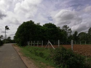 Empty road amidst trees on field against sky