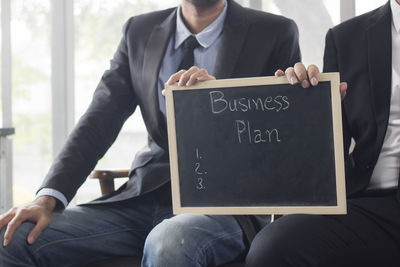 Midsection of business people holding slate while sitting on chair