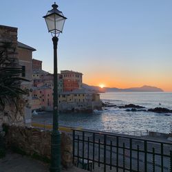 Street light by sea against buildings in city during sunset