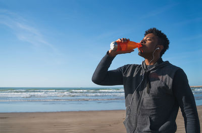 Full length of man drinking water at beach against sky