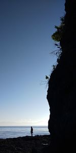 Silhouette people on rock by sea against clear sky