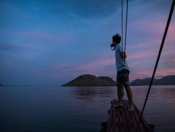 Full length of man photographing while standing on pier against sky during sunset